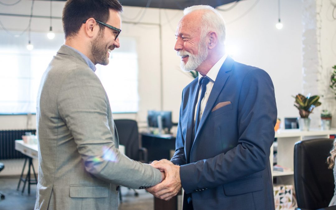 Senior executive shaking hands with young employee at office